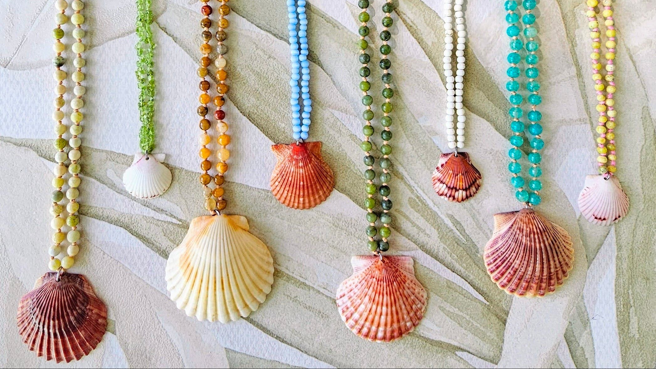 Set of six beaded necklaces with shell pendants on a textured surface