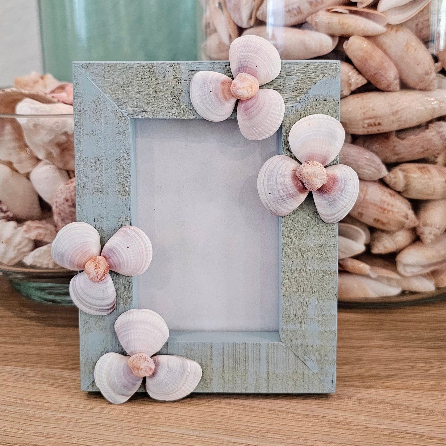 Decorative photo frame with shell embellishments on a wooden surface.