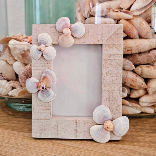 Decorative photo frame with shell embellishments on a wooden surface.