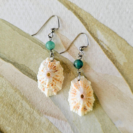 Shell and green bead earrings on a textured beige surface