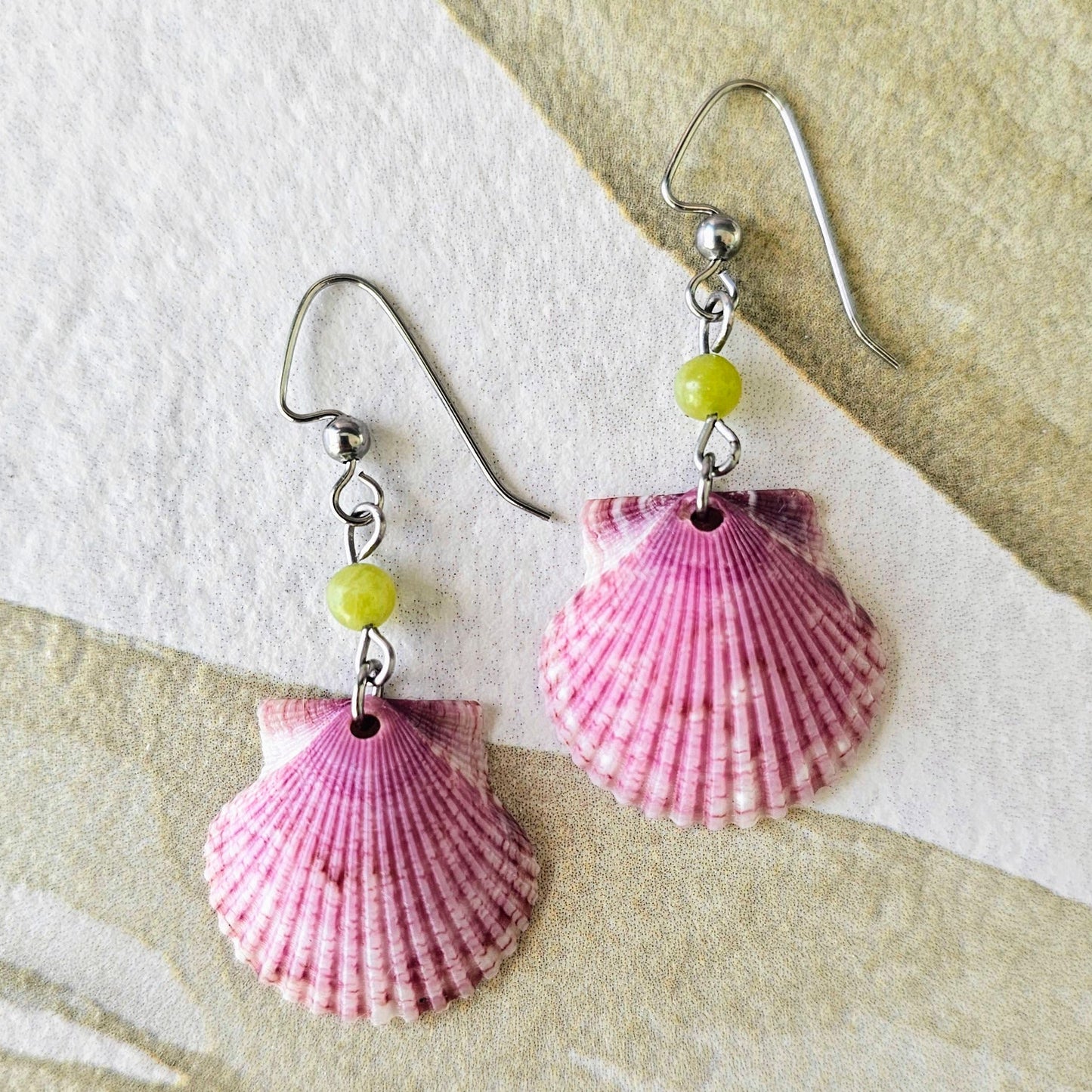 Shell-shaped earrings with pink and red patterns on a textured surface